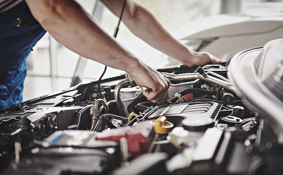 An image of a factory certified service technician performing routine engine maintenance on a vehicle in a repair bay. 