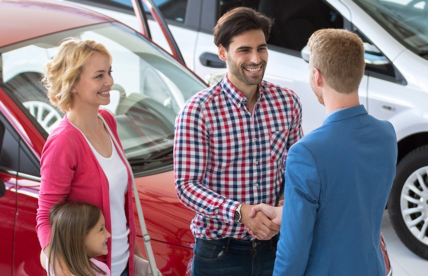 A happy family shaking the hand of their finance agent at a local dealership after finalizing the purchase of their new car.