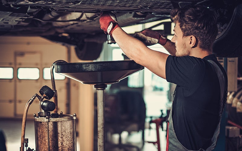 A service technician performing an oil change on a vehicle that is up on racks in a bay.