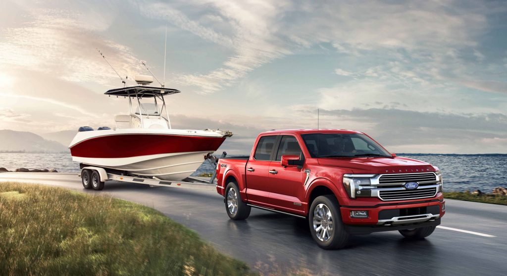 An image of a red Ford F-150 towing a boat along the highway next to the ocean.